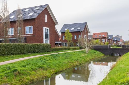 Enkele huizen met zonnepanelen in een wijk met een beek