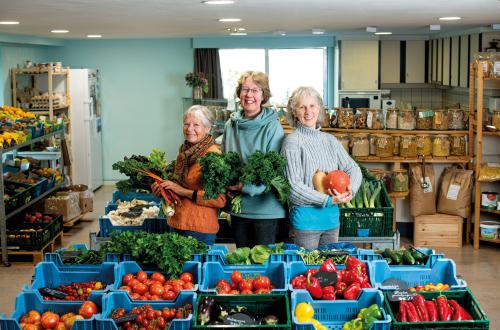 Drie dames tonen trots groenten en fruit in hun samenwinkel. 