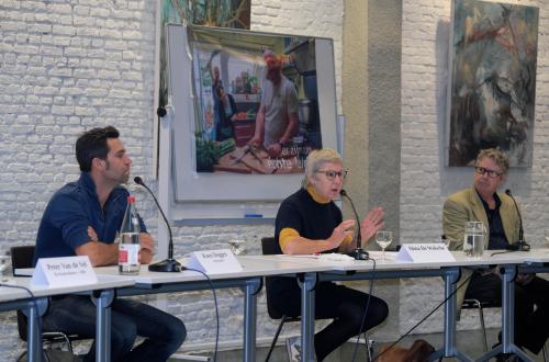 3 mensen zitten als een panel aan tafel en geven uitleg. 