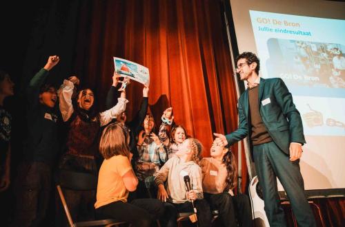 Kinderen juigen op een podium bij het winnen van een prijs. 