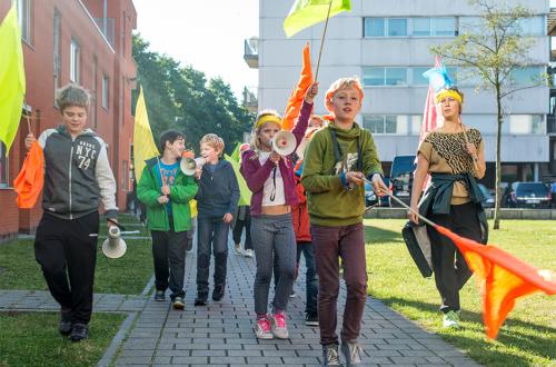 Een groep kinderen loopt met kleurrijk vlaggen door een straat. 