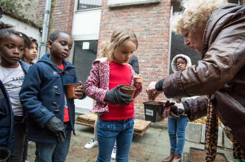 vrouw toont kinderen plantjes te verpotten