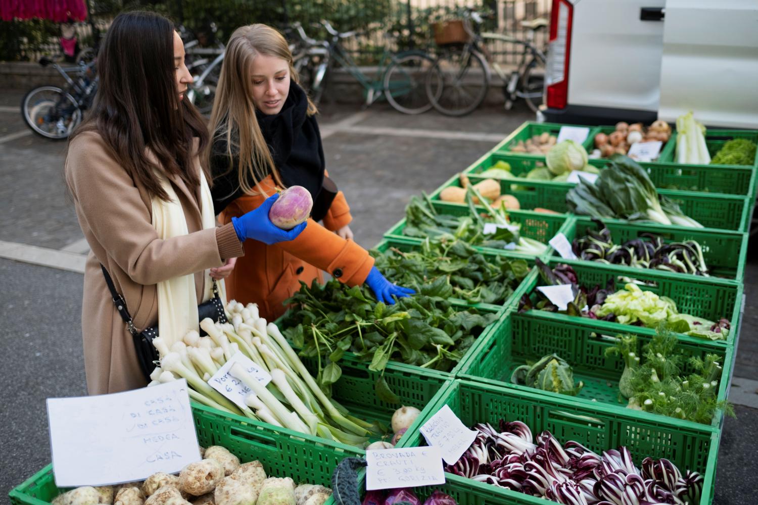 Twee vrouwen bekijken groenten van een groentekraam. 
