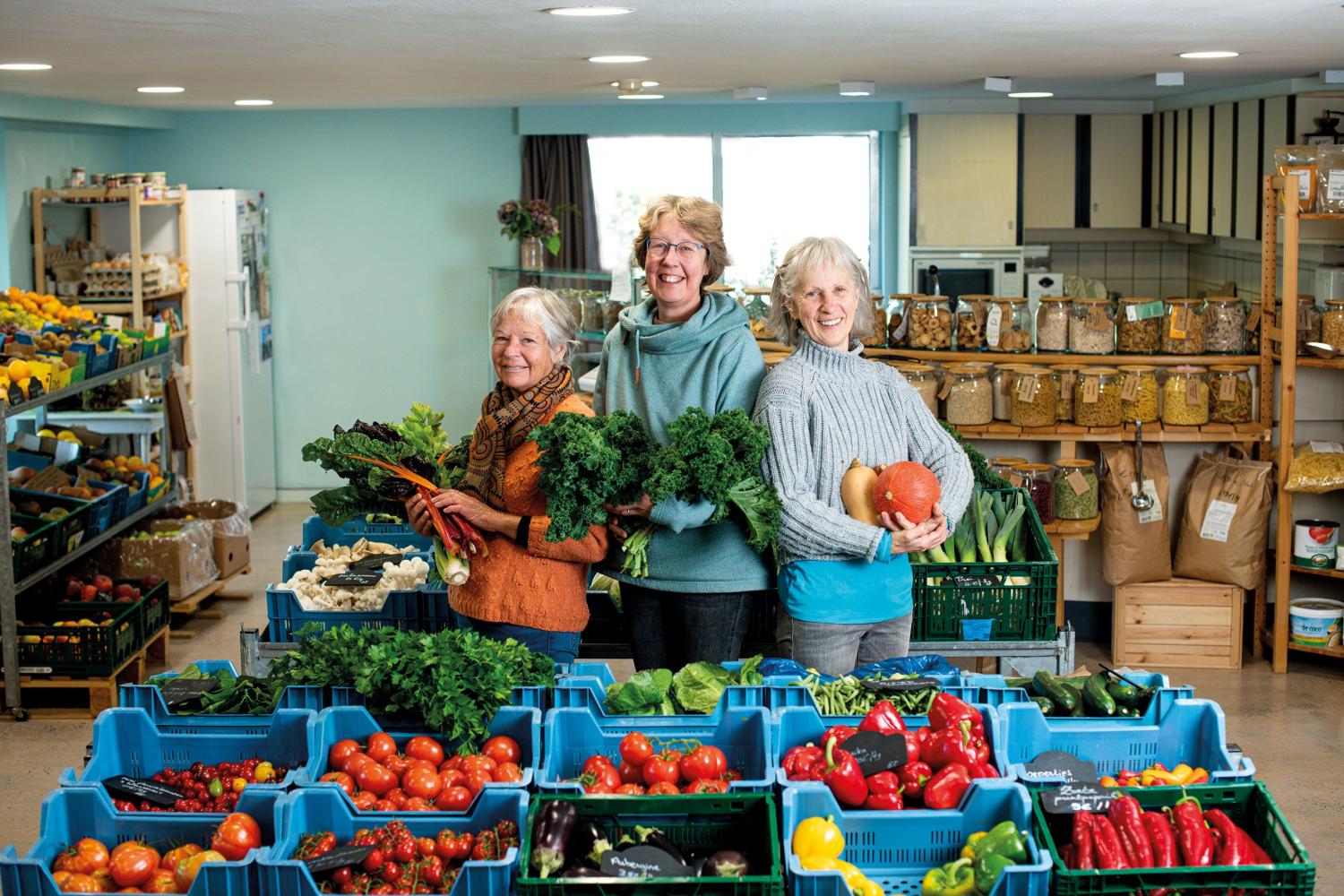 Drie dames tonen trots groenten en fruit in hun samenwinkel. 