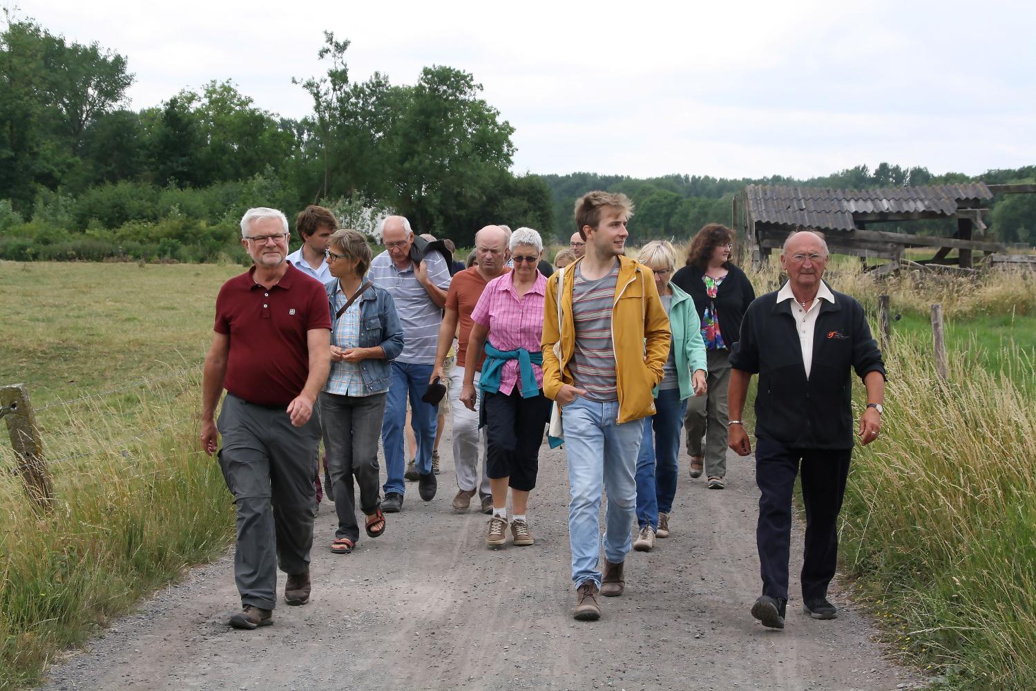Een groep mensen wandelt langs groene velden. 
