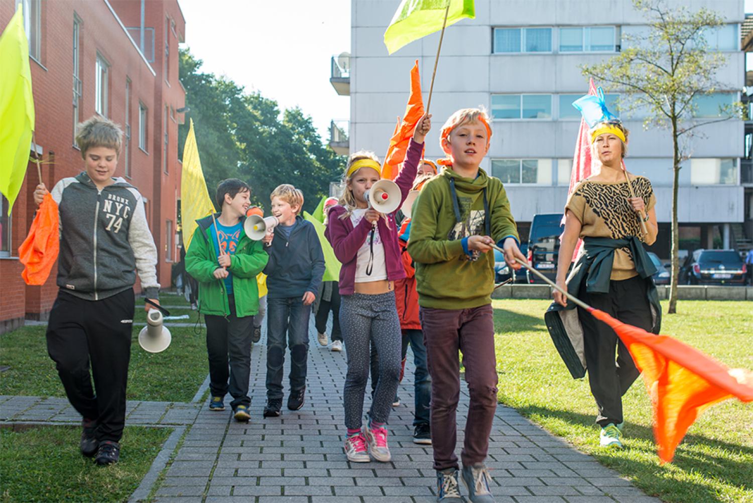 Een groep kinderen loopt met kleurrijk vlaggen door een straat. 