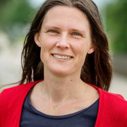 Een portretfoto van een jonge vrouw met bruin haar, een blauwe t-shirt en een rode pull
